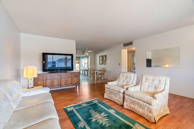 living room featuring ceiling fan, a textured ceiling, and light hardwood / wood-style flooring