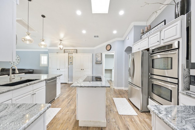 kitchen featuring stainless steel appliances, ornamental molding, a kitchen island, a sink, and white cabinetry