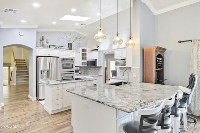 kitchen with stainless steel appliances, a sink, crown molding, a kitchen island, and a skylight