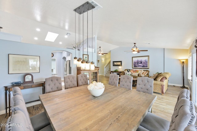dining room featuring vaulted ceiling, ceiling fan, arched walkways, wood finished floors, and a skylight