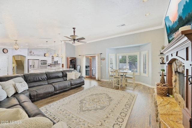 living area with a fireplace with raised hearth, arched walkways, crown molding, ceiling fan, and light wood-type flooring