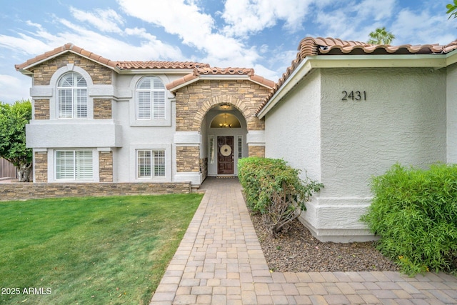 entrance to property with stucco siding, stone siding, a yard, and a tile roof