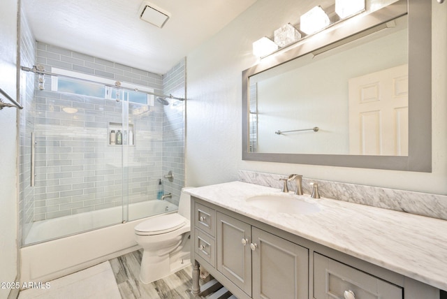 bathroom with toilet, vanity, and bath / shower combo with glass door