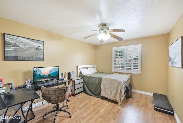 bedroom featuring light wood finished floors, baseboards, an office area, a textured ceiling, and ceiling fan