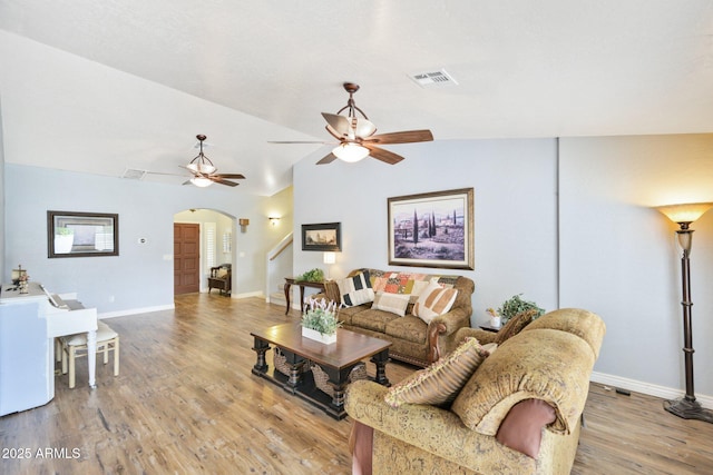 living area featuring arched walkways, ceiling fan, light wood-type flooring, baseboards, and vaulted ceiling