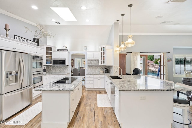 kitchen featuring appliances with stainless steel finishes, a sink, ornamental molding, a peninsula, and light wood finished floors