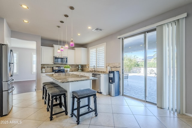 kitchen with light stone countertops, white cabinets, a center island, decorative light fixtures, and stainless steel appliances