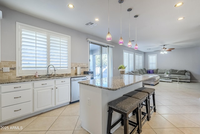 kitchen with light stone countertops, pendant lighting, dishwasher, white cabinetry, and a breakfast bar