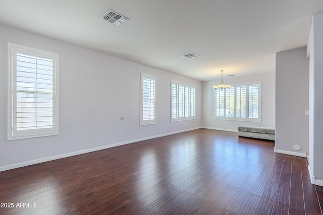 spare room with an inviting chandelier and dark hardwood / wood-style flooring