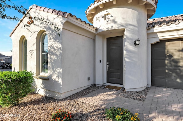 property entrance with a tiled roof, stucco siding, and an attached garage