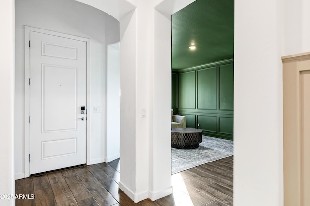 entrance foyer featuring dark wood finished floors, a decorative wall, and baseboards