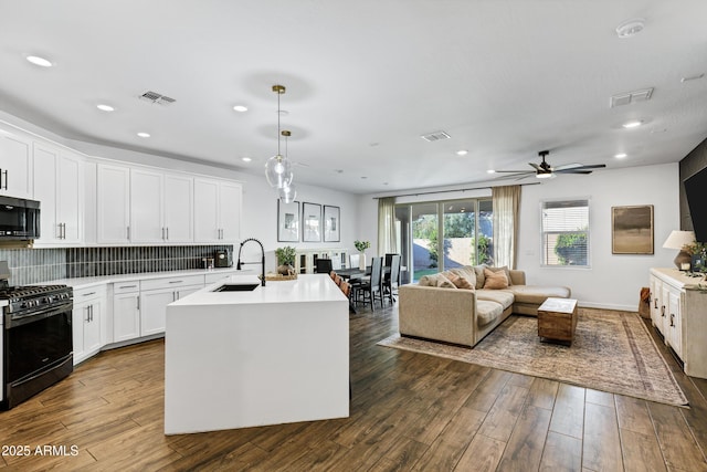 kitchen with black gas stove, a sink, stainless steel microwave, open floor plan, and light countertops