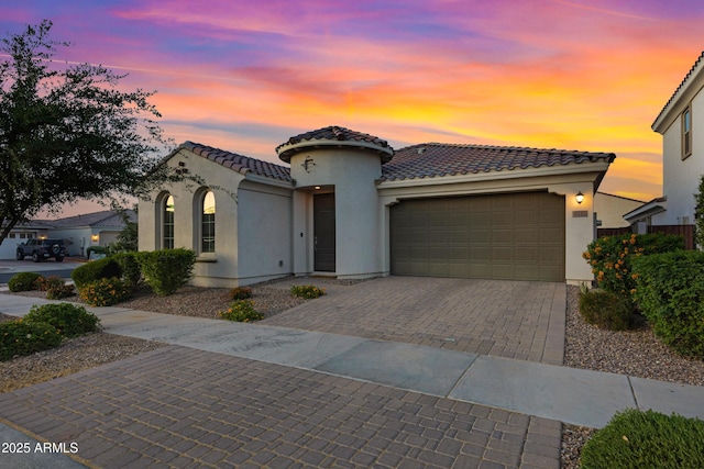 mediterranean / spanish house featuring decorative driveway, a tiled roof, an attached garage, and stucco siding