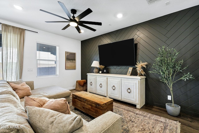 living area with a ceiling fan, wood finished floors, an accent wall, baseboards, and recessed lighting