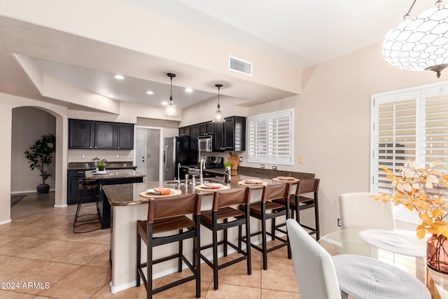 kitchen with stainless steel appliances, light tile patterned floors, a breakfast bar, pendant lighting, and dark stone countertops