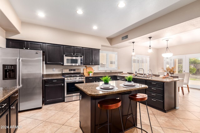 kitchen featuring light stone counters, appliances with stainless steel finishes, decorative light fixtures, a breakfast bar, and a center island