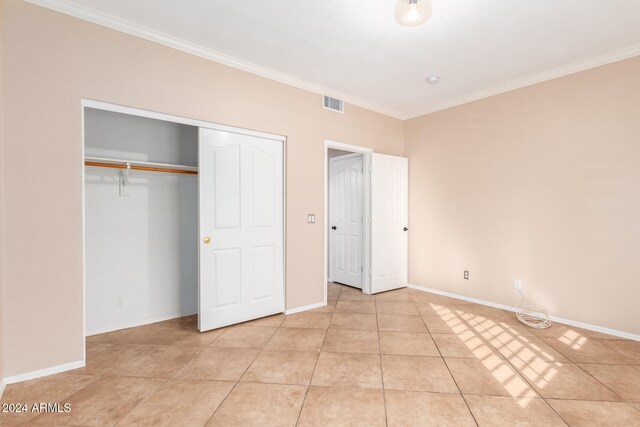 unfurnished bedroom with light tile patterned flooring, a closet, and crown molding