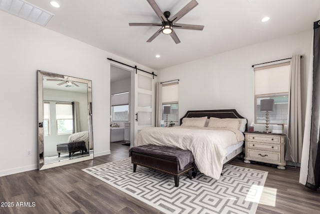 bedroom with a barn door, dark wood-style floors, recessed lighting, baseboards, and ensuite bath