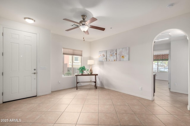 foyer entrance with light tile patterned flooring, baseboards, arched walkways, and ceiling fan