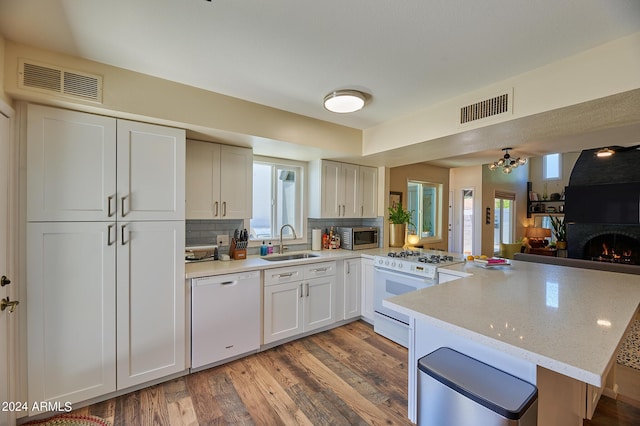 kitchen featuring tasteful backsplash, wood-type flooring, sink, kitchen peninsula, and white appliances