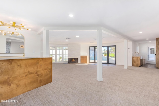 unfurnished living room with a chandelier, light carpet, a large fireplace, and plenty of natural light