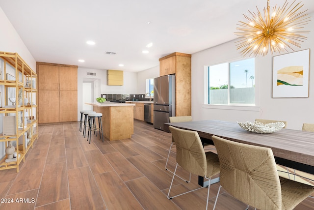 kitchen with a center island, backsplash, appliances with stainless steel finishes, a notable chandelier, and wood-type flooring