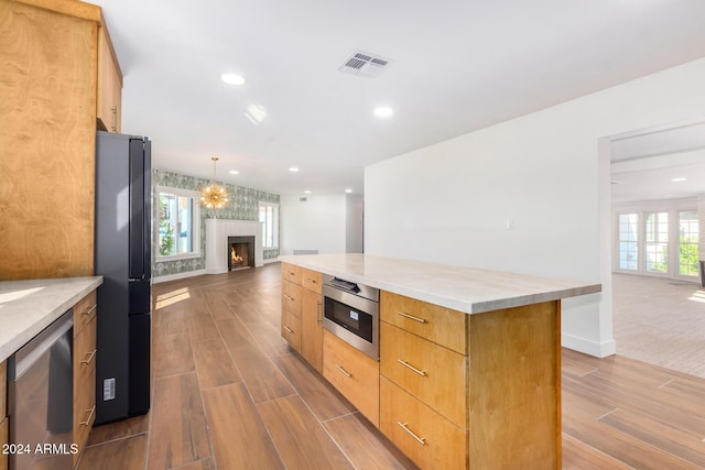 kitchen with a center island, black fridge, hanging light fixtures, stainless steel dishwasher, and light hardwood / wood-style floors