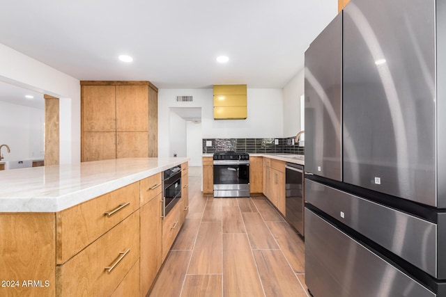 kitchen with light stone counters, stainless steel appliances, a spacious island, sink, and light hardwood / wood-style flooring