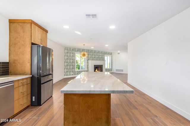 kitchen with light stone countertops, stainless steel appliances, decorative light fixtures, light hardwood / wood-style flooring, and a fireplace