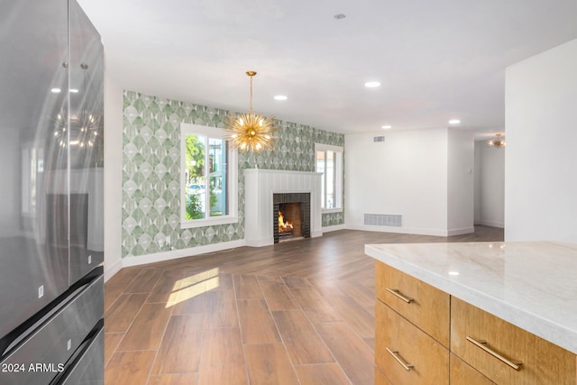 unfurnished living room with an inviting chandelier, a brick fireplace, and dark wood-type flooring