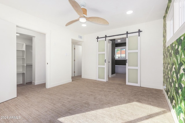 unfurnished bedroom featuring light carpet, ceiling fan, a barn door, a spacious closet, and a closet