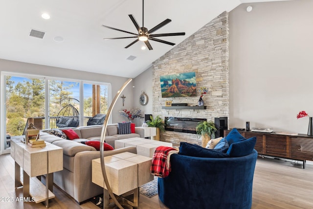 living room featuring a stone fireplace, high vaulted ceiling, ceiling fan, and light wood-type flooring