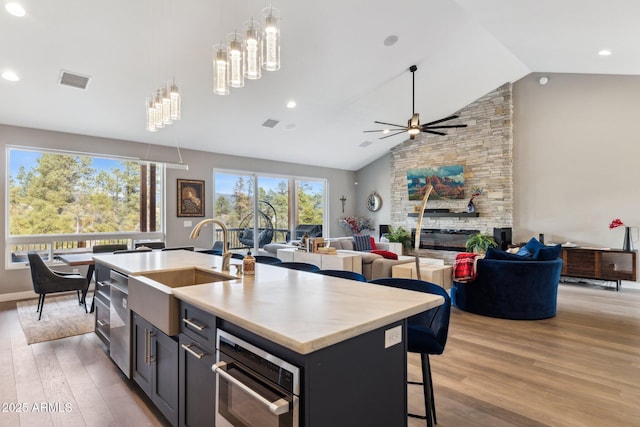 kitchen with a breakfast bar, light wood-type flooring, pendant lighting, a fireplace, and a kitchen island with sink