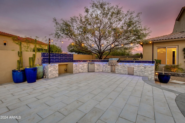 patio terrace at dusk featuring grilling area, pool water feature, and exterior kitchen