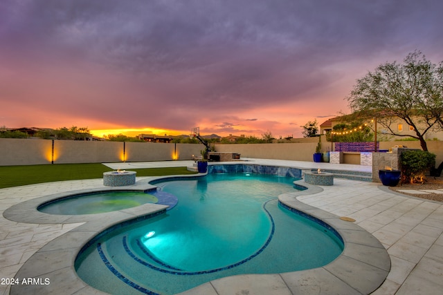 pool at dusk with a patio and an in ground hot tub