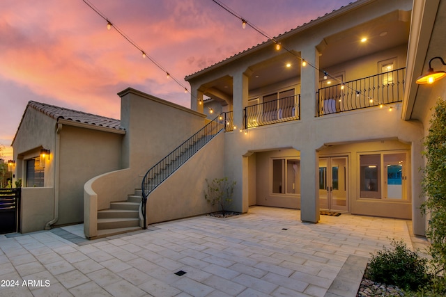 back house at dusk featuring a balcony and a patio