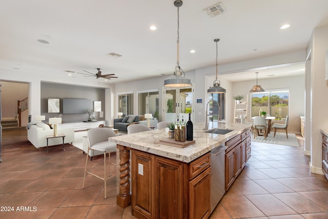 kitchen featuring pendant lighting, ceiling fan, a center island with sink, stainless steel dishwasher, and sink