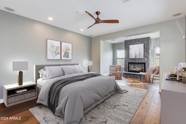 bedroom with ceiling fan, a stone fireplace, and hardwood / wood-style flooring