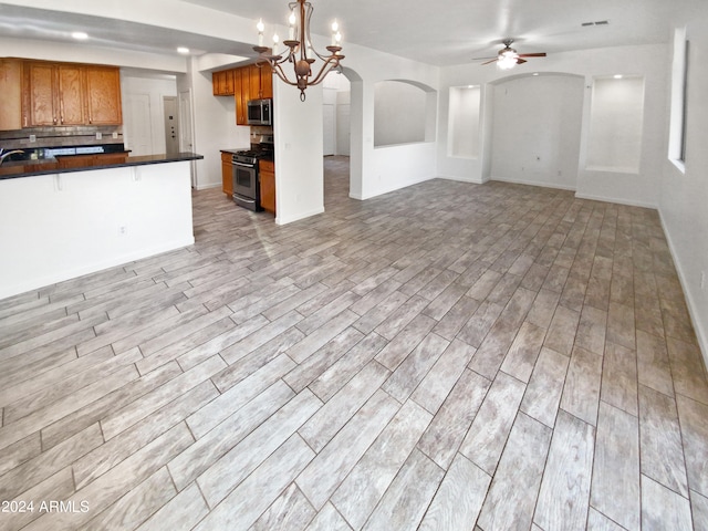 unfurnished living room with ceiling fan with notable chandelier and light hardwood / wood-style floors