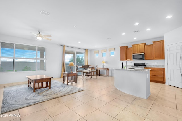 kitchen with light stone countertops, stainless steel appliances, ceiling fan, a kitchen island with sink, and light tile patterned floors