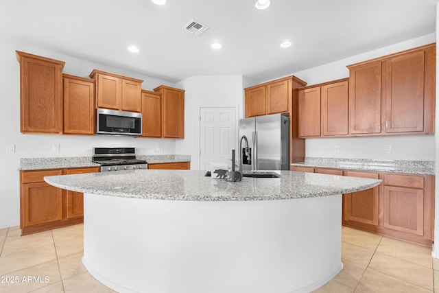 kitchen with light stone counters, light tile patterned floors, stainless steel appliances, and an island with sink