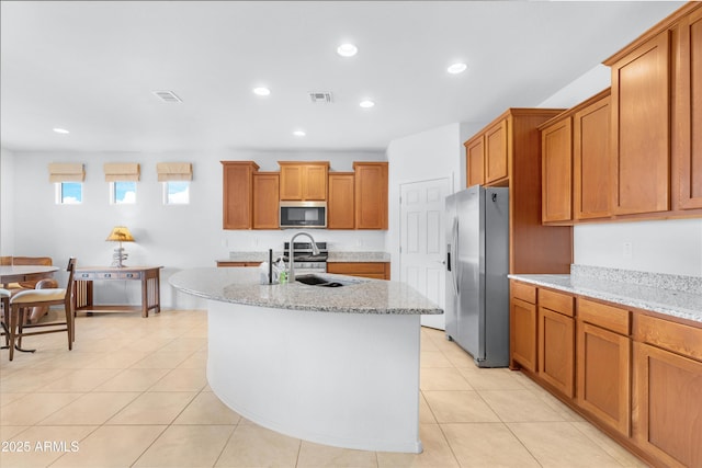 kitchen with light stone counters, sink, an island with sink, and stainless steel appliances