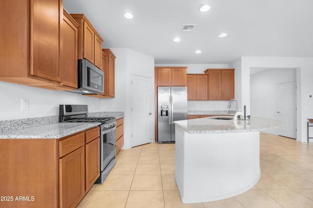 kitchen featuring sink, light stone counters, a center island with sink, light tile patterned floors, and appliances with stainless steel finishes