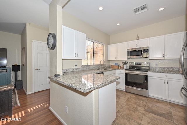 kitchen with sink, white cabinetry, stainless steel appliances, light stone countertops, and kitchen peninsula