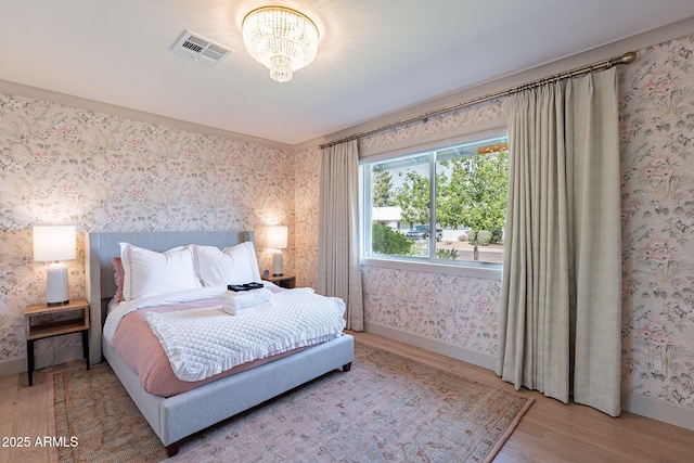 bedroom with baseboards, visible vents, wood finished floors, and wallpapered walls