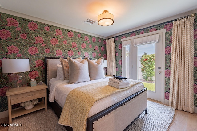 bedroom with access to outside, wallpapered walls, wood finished floors, and visible vents