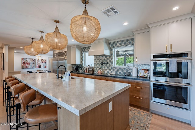 kitchen with custom exhaust hood, a sink, decorative backsplash, stainless steel appliances, and visible vents