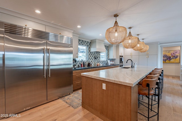 kitchen with light wood finished floors, built in fridge, custom exhaust hood, and decorative backsplash