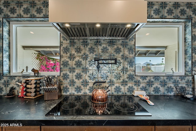 details with dark countertops, wall chimney exhaust hood, black electric stovetop, and wallpapered walls