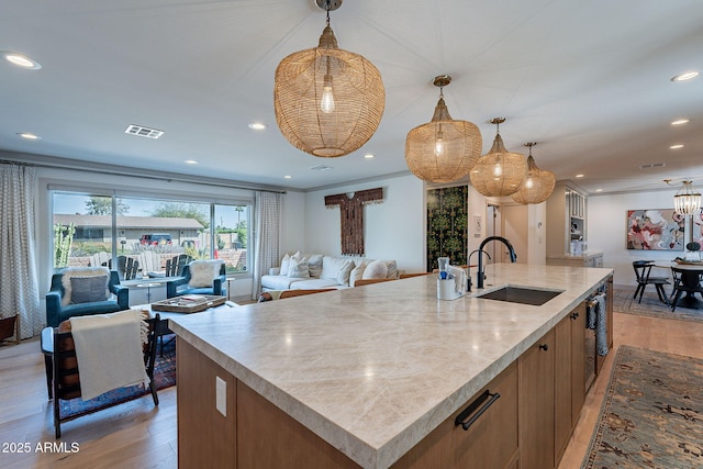 kitchen with a sink, an island with sink, open floor plan, light wood-style floors, and visible vents